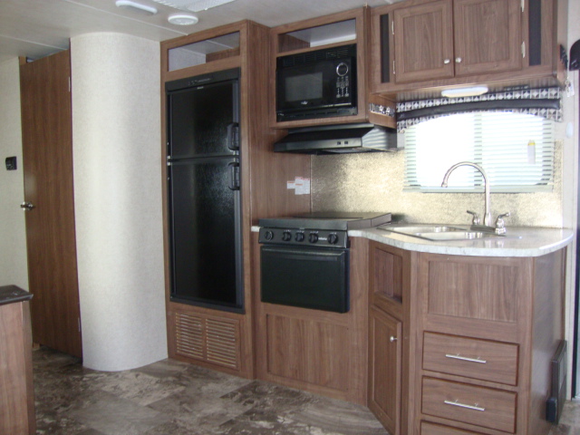 The Pioneer RL250 travel trailer features a fully-equipped kitchen with a fridge, microwave oven, sink, and grill setup